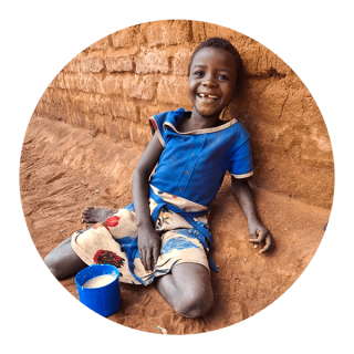 Dítě sedí na zemi s hrnkem kaše a usmívá se