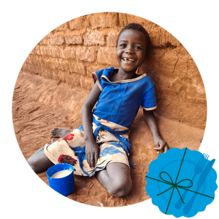 Dítě sedí na zemi s hrnkem kaše a usmívá se